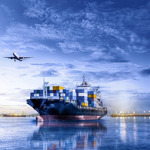 Container ship carrying freight at sea with an aircraft flying overhead